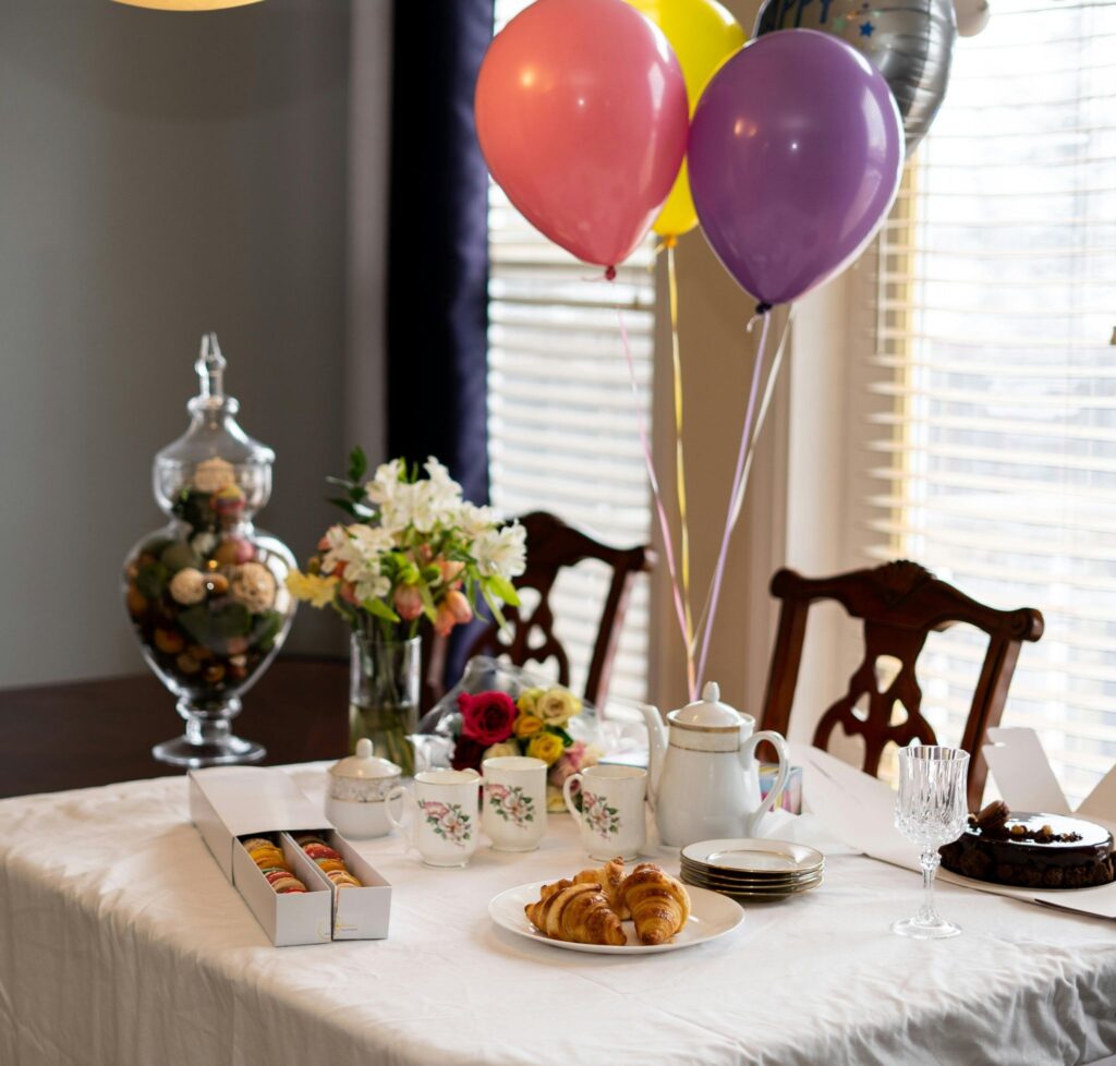 Un florero con tulipanes naranjas junto a unos hot cakes con fresas y un letrero de “¡Feliz Día Mamá!” sobre una mesa.